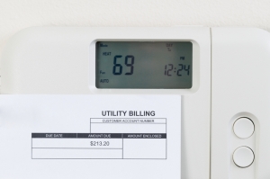 Close up of home heating thermostat with partial utility bill on wall.